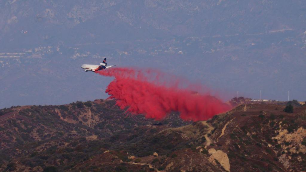 An image showing an airtanker dropping bright red fire retardant onto hills in California 