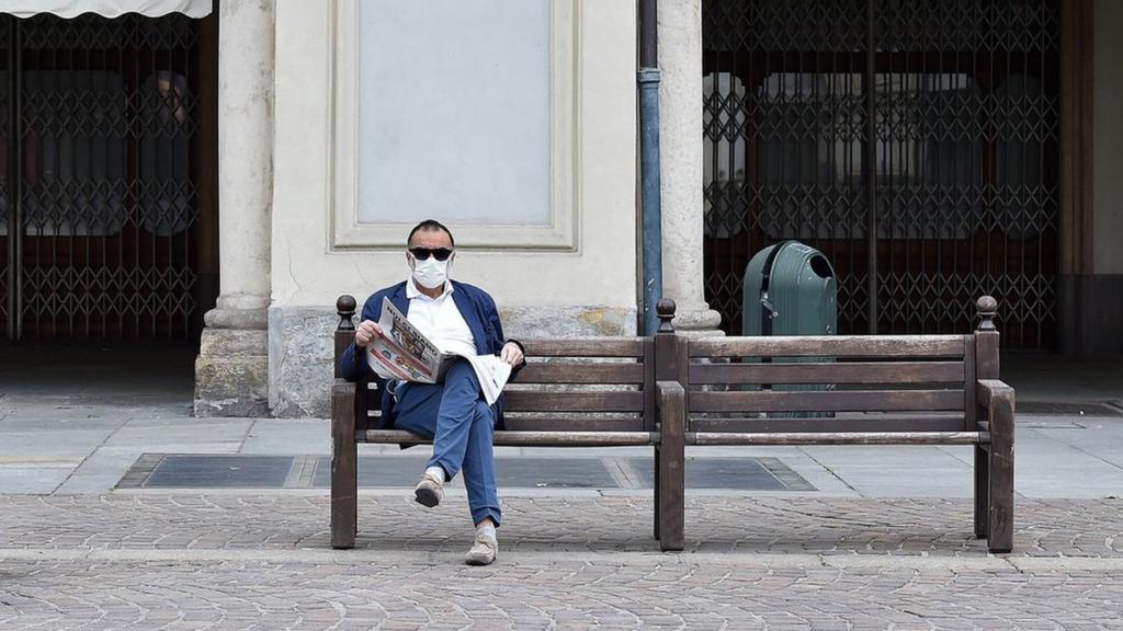 A man sitting on a bench in an empty street reads the newspaper in Turin, Italy, 19 April 2020. Countries around the world are taking increased measures to stem the widespread of the SARS-CoV-2 coronavirus which causes the Covid-19 disease