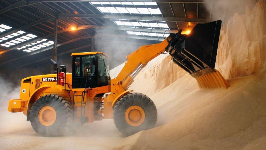 Excavator moving fertilizer in a warehouse on the dockside at a port in Newport, South Wales