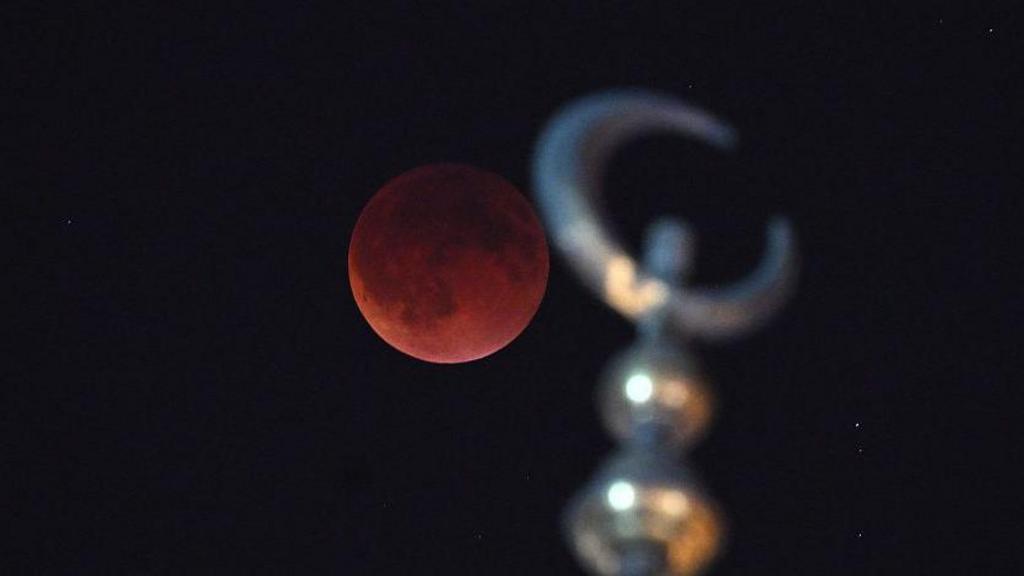 A full moon, also known as the "Blood Moon," is pictured above a minaret in Kuwait City on September 7, 2025