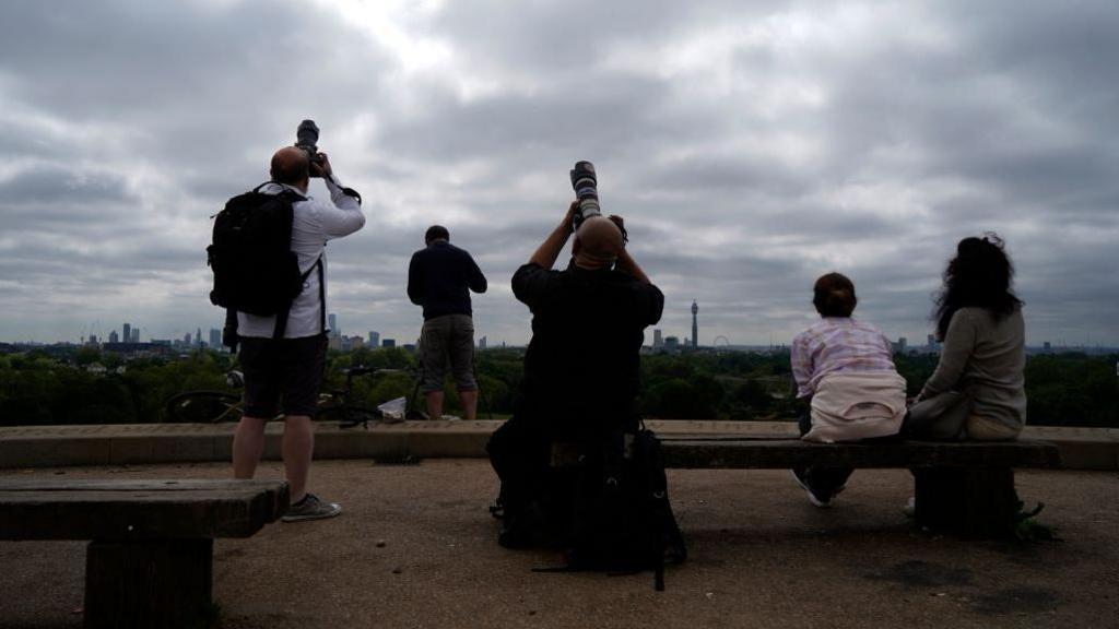 People watch the sky from Primrose Hill in north London as photographers aim cameras towards the horizon.
