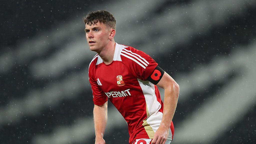 Gavin Kilkenny playing for Swindon Town during a rainy match. A poppy armband is clearly visible, worn on his left arm.