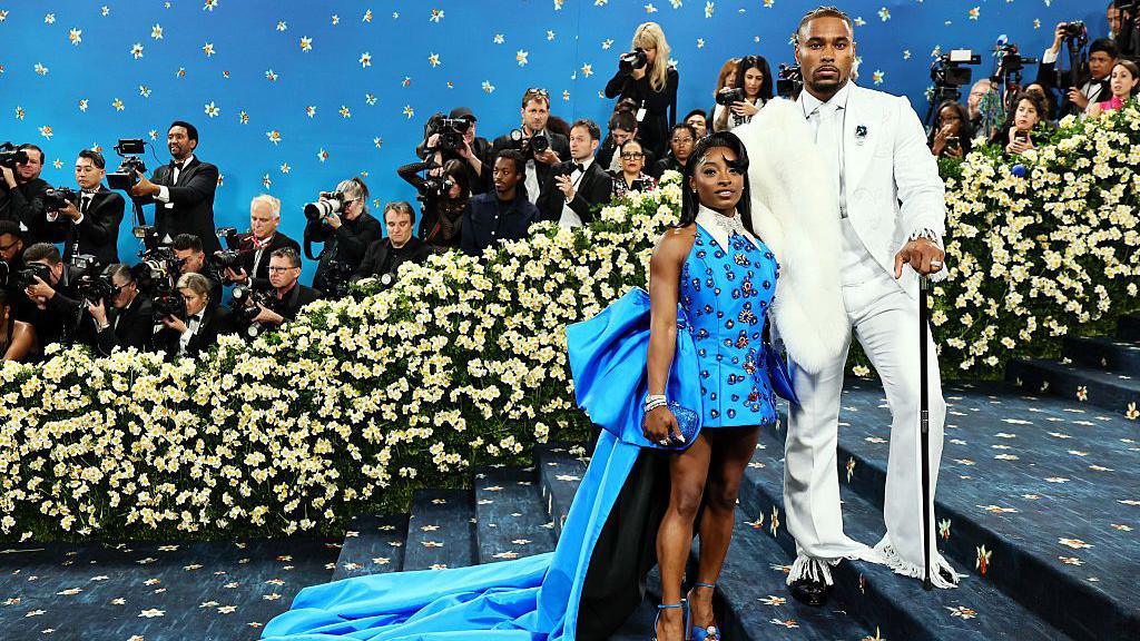 Simone Biles and Jonathan Owens attend the 2025 Met Gala, Simone wears a blue beaded dress whilst Jonathon wears a white suit.
