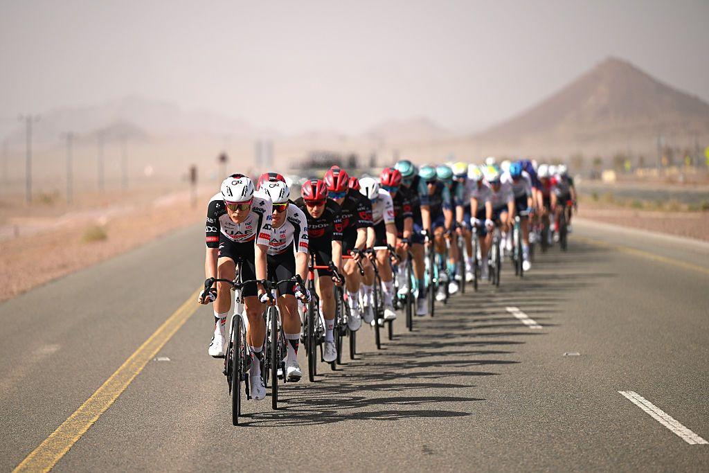 Danish cyclist Julius Johansen and UAE Team race along a long, open desert road, riding nose to tail in formation, heat haze and distant mountains.