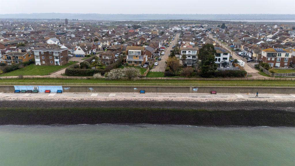 An aerial photo showing the sea in the foreground and rows of houses in the background. It is cloudy.