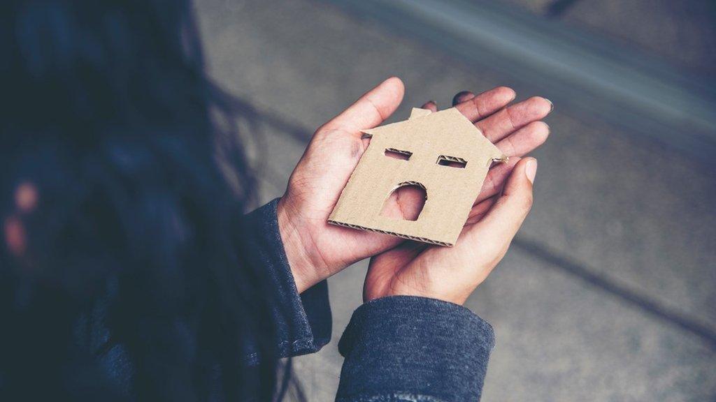 A woman holding a small cardboard house cutout