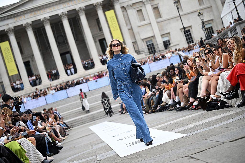 A woman dressed in light blue denim walks down a catwalk in Trafalgar Square, London.
