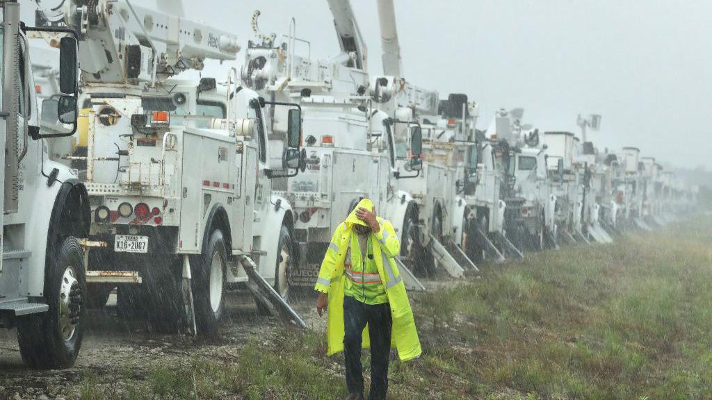 Charles Starling, a lineman with Team Fishel, is pelted with rain as he walks by a row of electrical line trucks staged in a field in The Villages, Florida 