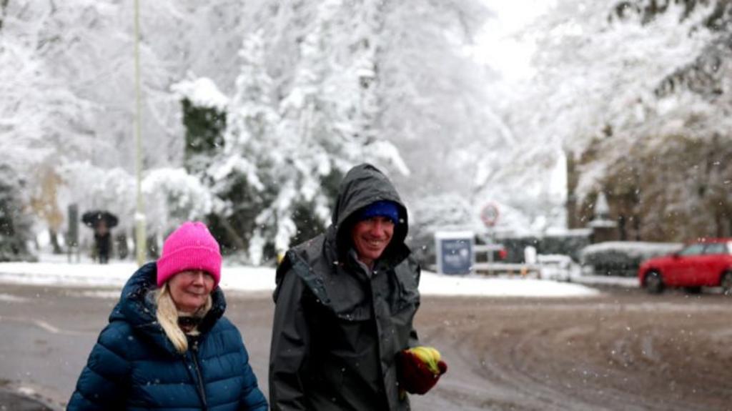 People walk through street covered in snow wearing hats and coats