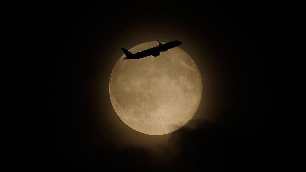 Bright full Moon with a silhouetted plane flying in front of it 