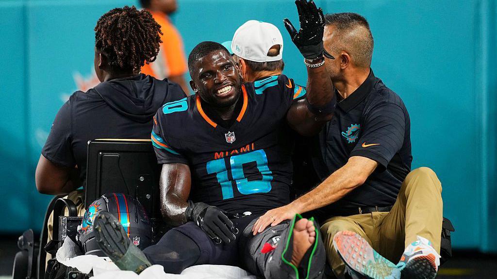 Tyreek Hill smiles and waves as he sits on a buggy