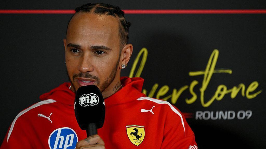 Lewis Hamilton holds a microphone while answering questions in the news conference at Silverstone