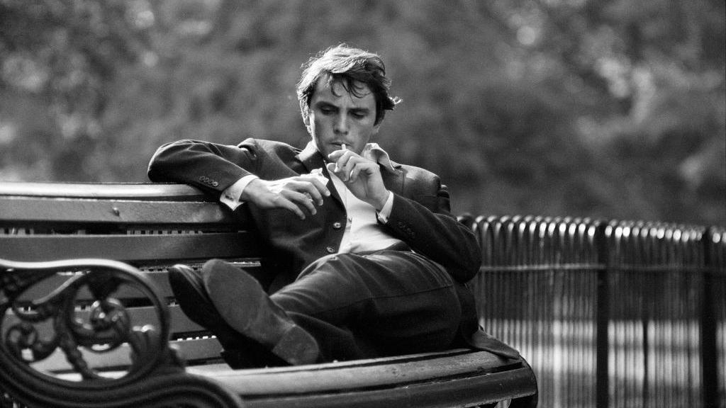 Terence Stamp sitting smoking on a park bench