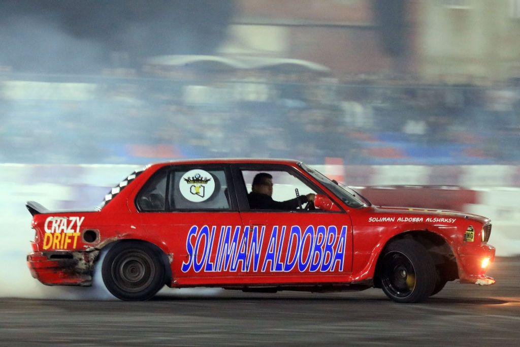 A red car speeds along a track during a drifting showcase - the crowd in the background are blurred because of the speed.