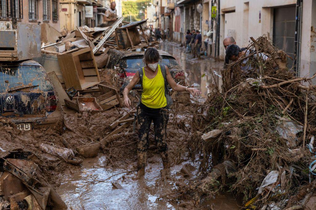 A woman walks along a street full of mud and waste from houses after heavy rain and flooding