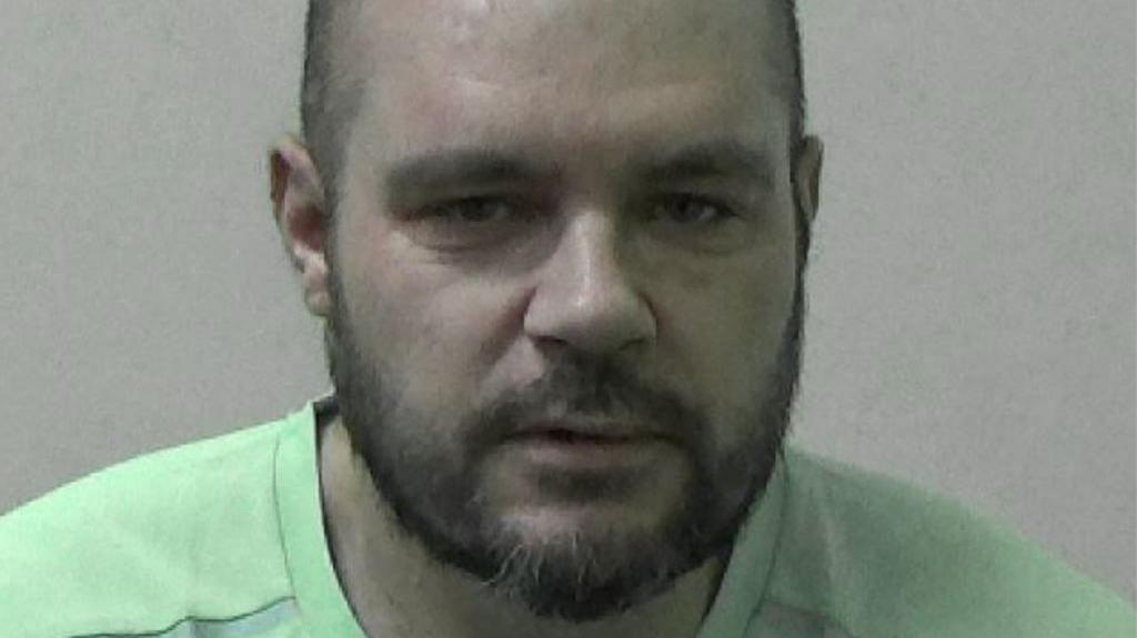 Mugshot of a man with a round head and short dark beard