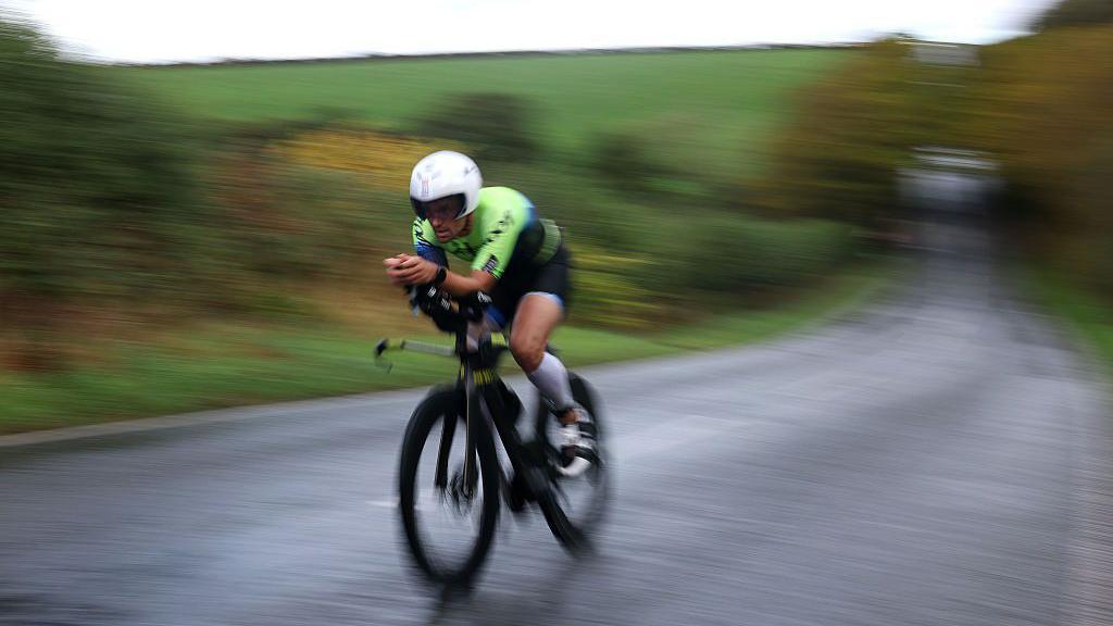 A cyclist appears blurred as he speeds past the camera on a country road
