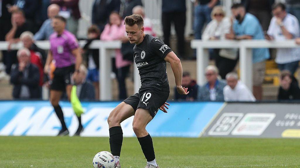 Boreham Wood's Tom White, wearing an all black kit, plays a pass during a game for the National League club