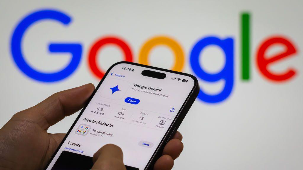 Hand holding a Google phone, using the Gemini AI application, with a lit up Google logo on the wall in the background