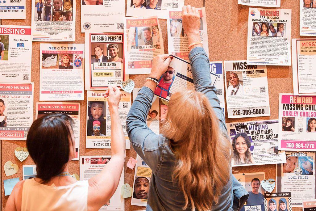 Two women look at a board filled with missing people posters