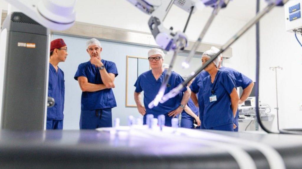 Equipment is in the foreground and the four people are in health uniform in the background, along with two others whose faces are not visible.