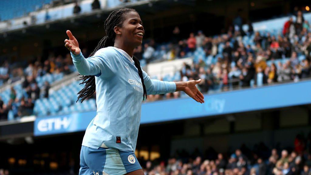 khadija shaw celebrating on the pitch with the crowd out of focus behind her
