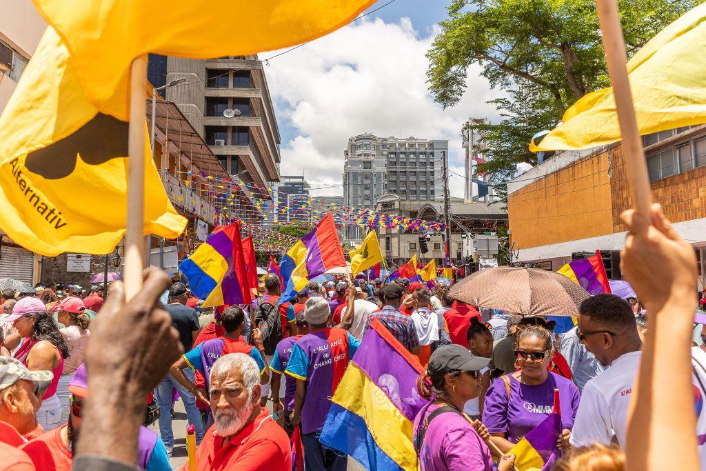 Change Alliance supporters in mainly red, purple T-shirt hold flags as they gather to attend a campaign rally - bunting in the party colours - purple, yellow, red and blue - can also be seen in Port Louis, Mauritius - Sunday 3 November 2024