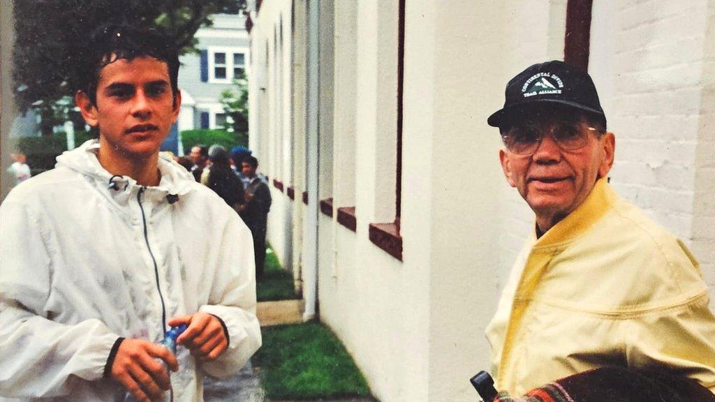 A teenager Felipe Nystrom, dressed in a white tracksuit top, stands next to his grandfather