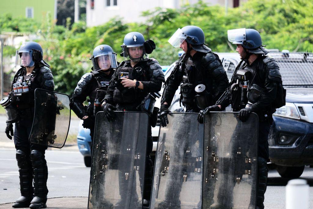 Five police officers in riot gear standing in front of car in Nouméa 