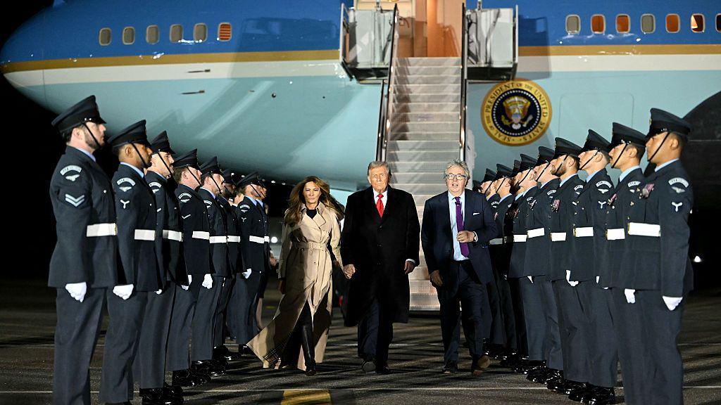 US President Donald Trump and US First Lady Melania Trump disembark from Air Force One with a line of army personnel on each side