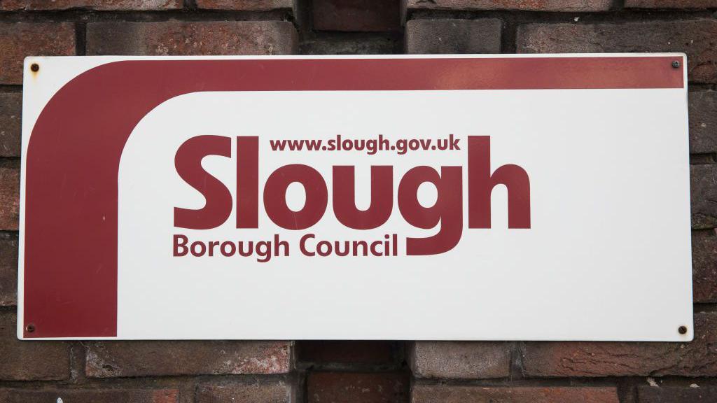 A red and white sign for Slough Borough Council attached to a brick wall.