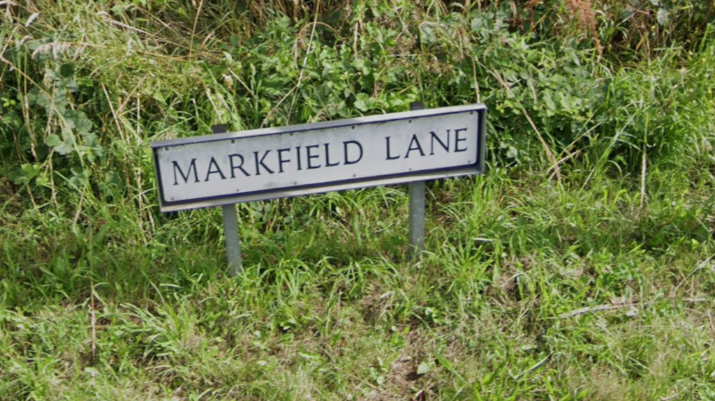 A street sign saying Markfield Lane with grass around the sign