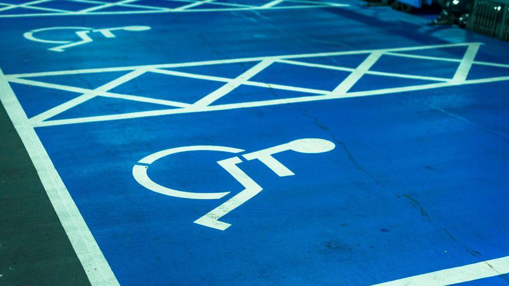 A closeup photograph of a blue painted disabled parking bay. There are white hatching lines to separate the parking bays.