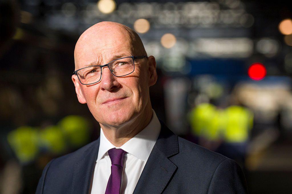John Swinney, a bald man with glasses wearing a dark suit and a purple tie