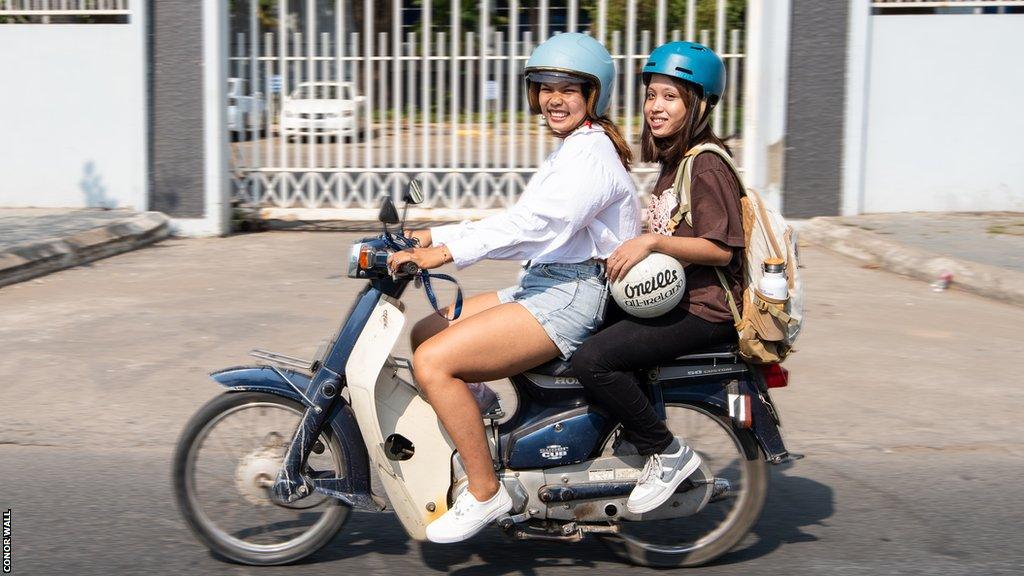 Vat Sreypov and Ava ride a moped to training