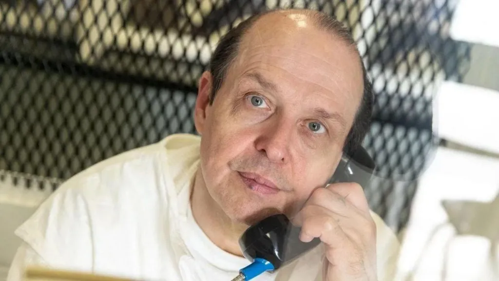 Robert Roberson, in a white prison outfit, looks into the camera with a prison telephone at his ear