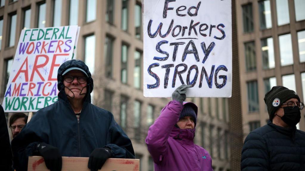 People protest with signs in support for US government workers. 