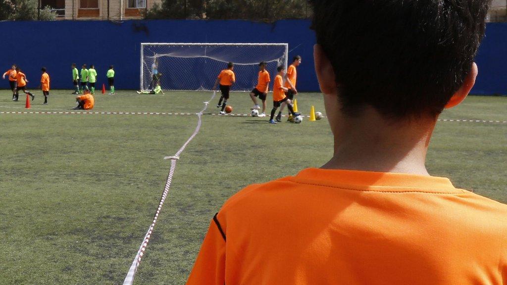 a youth footballer stands away from other players