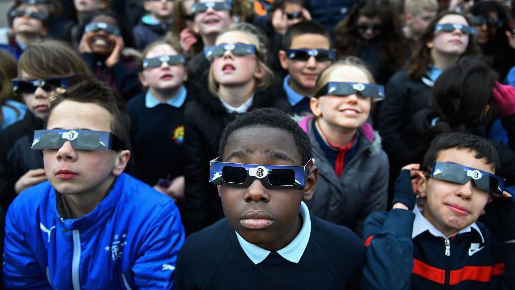 A group of children watching an eclipse wearing special protective glasses.