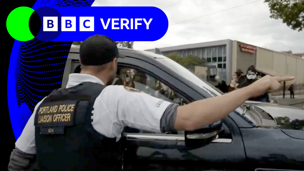 Man wearing vest which says "Portland Police Liaison Officer" is speaking into an open car window and pointing 