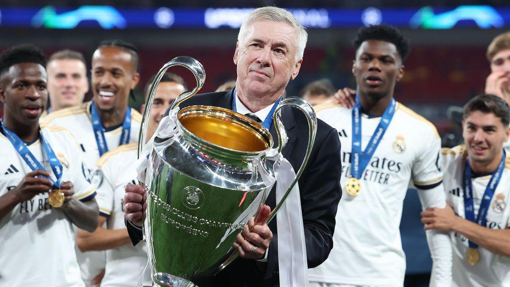 Carlo Ancelotti celebrates with the 2023-24 Champions League trophy, surrounded by his Madrid players.