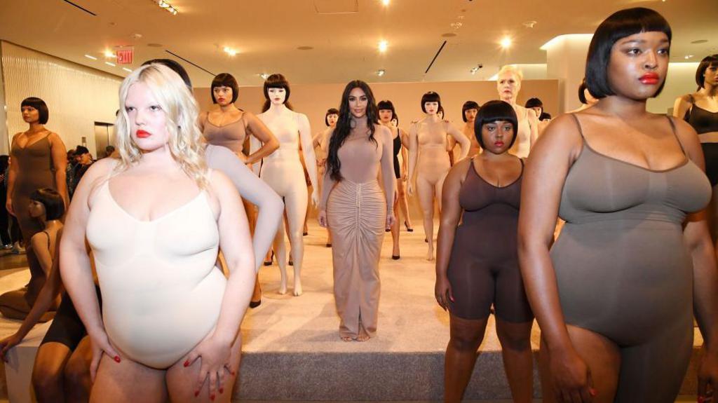 Kim Kardashian standing in a Skims store surrounded by women wearing her shapewear