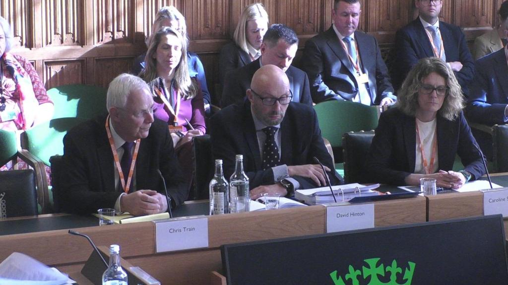 Three people sit at a committee hearing