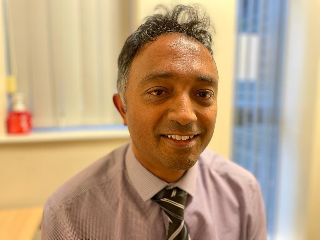 Dr Choudhary has dark hair and is wearing a shirt and tie.