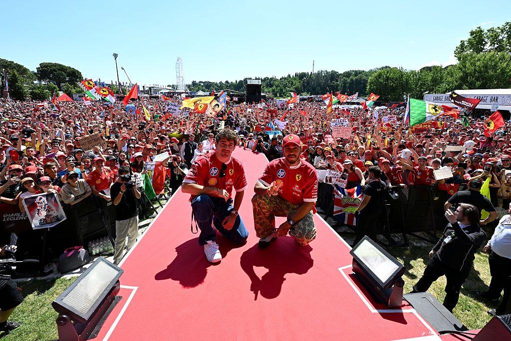 Charles Leclerc and Lewis Hamilton crouch on stage as they pose for a photograph with thousands of Ferrari fans in the background in Imola