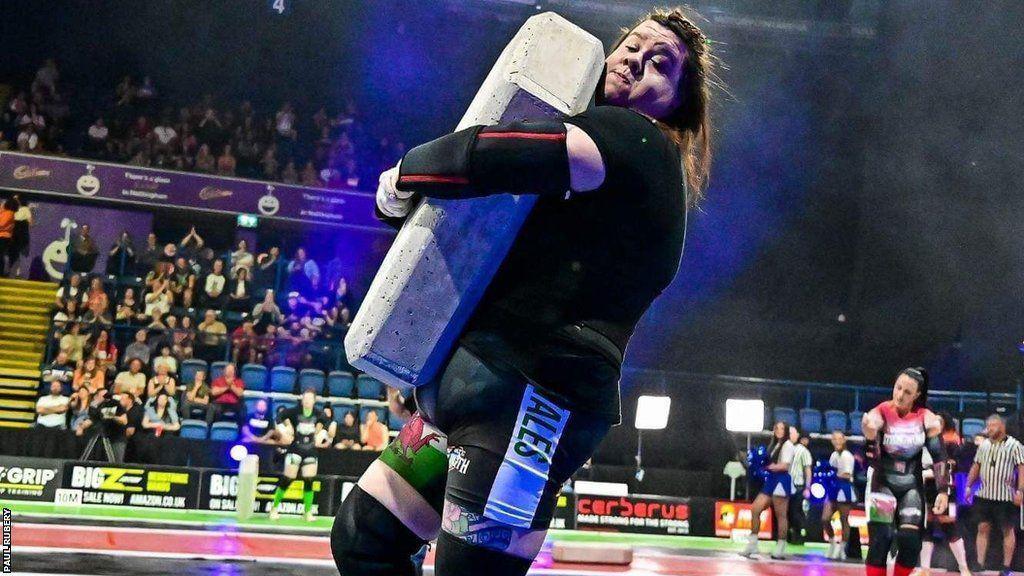 Rebecca straining as she carry's a concrete  block 