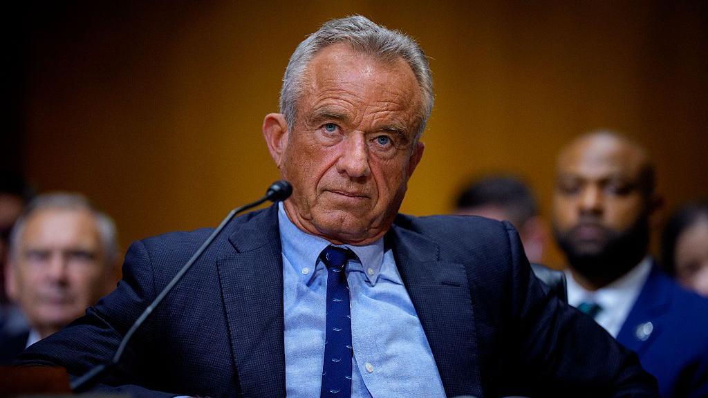 Robert F Kennedy Jr during a committee hearing. He is wearing a dark suit and tie with a blue shirt. 