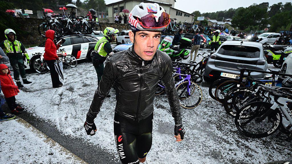 Wout van Aert looks at the camera as he walks away from his bike with hail covering the ground
