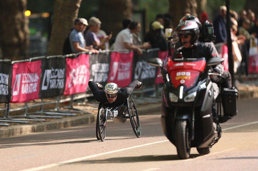 An elite wheelchair competitor dressed in black in the sun with BBC Sport motorbike in foreground - Marcel Hug of Team Switzerland competes during the Wheelchair T53/T54 race in the sunshine in 2025