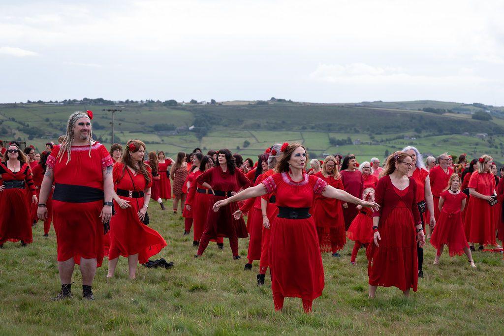 A group of women dressed in red dressed dance on the moors, many with their hands in the air, as part of an event to celebrate Kate Bush
